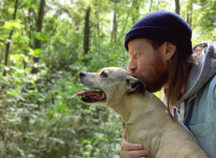 portrait of a man kissing his dog in the forest