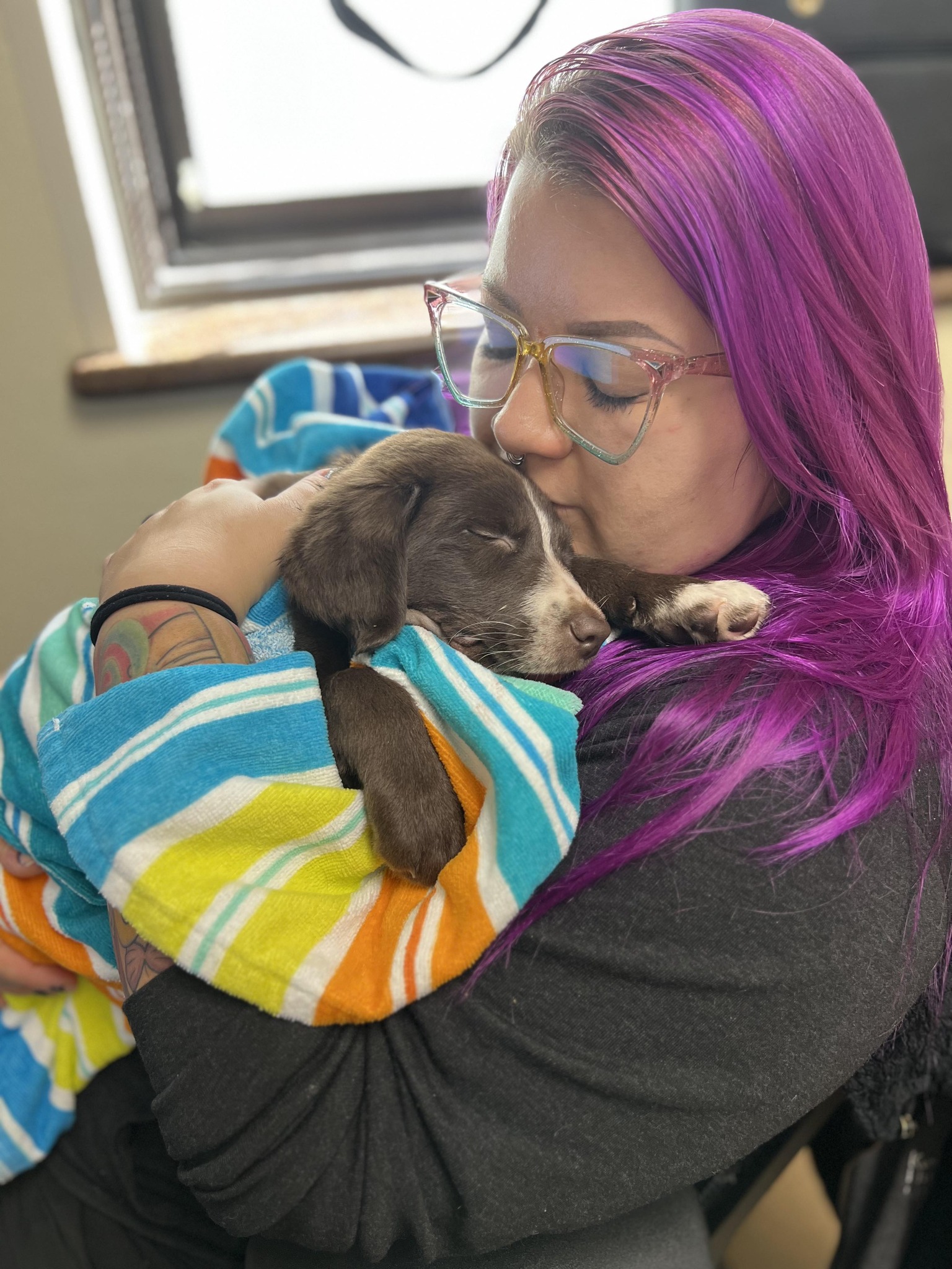 woman with purple hair kissing dog in arms